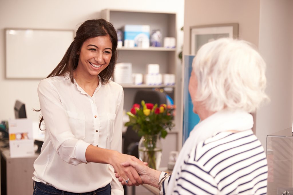 A female caregiver shaking hands with a senior woman.