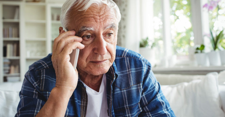 A senior man looking worried while talking on the phone.